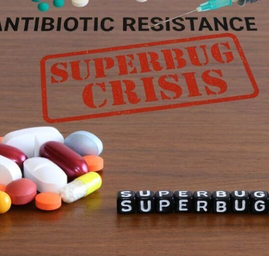 Realistic image showing medical supplies on a wooden surface with bold text "ANTIBIOTIC RESISTANCE", illustrating the superbug crisis.